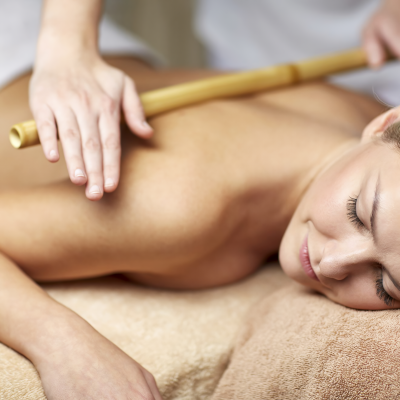 Девушка лежит на массажном столе, мастер раскатывает ее спину массажной бамбуковой палкой